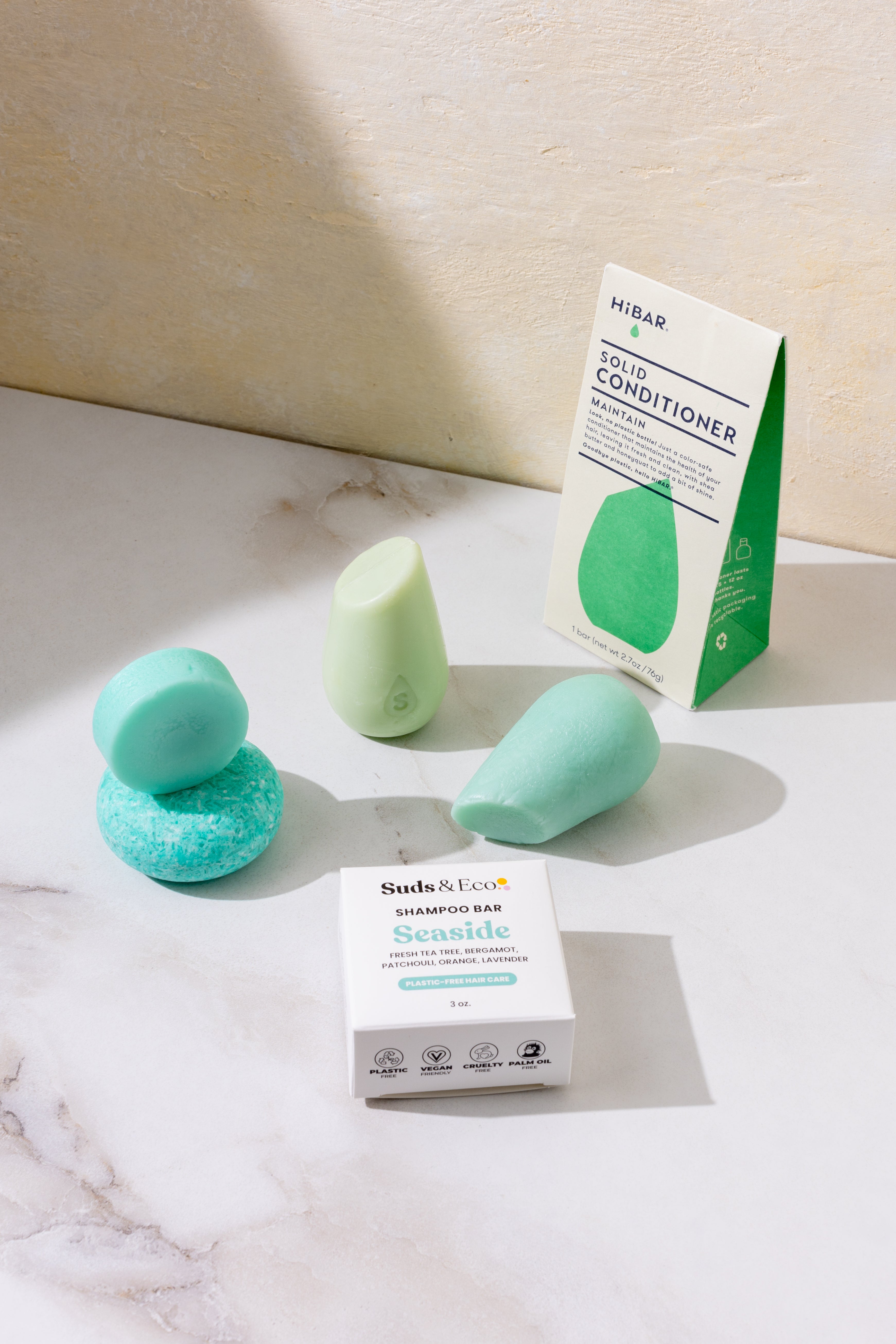 Green shampoo bars and their packaging on a marble surface with a neutral background